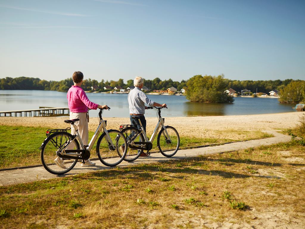 Man and woman walking next to bike, looking at lake